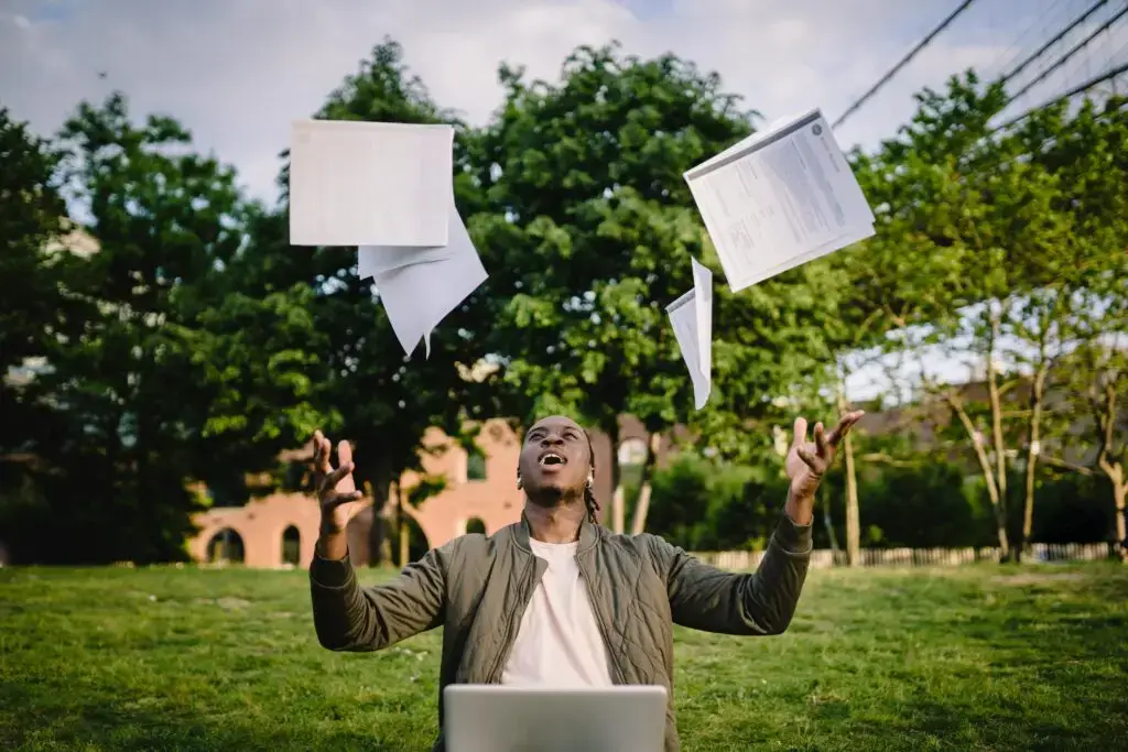Happy young black man throwing papers into the air while celebrating his decision to use a speaking coach to perform better in his oral exam.
