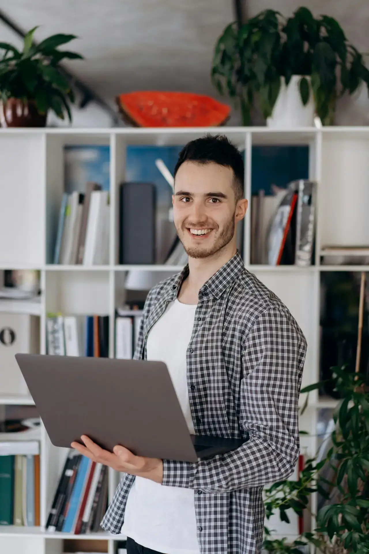 Young man holds a laptop in a modern indoor setting proud of his decision to invest in a personalised training course to perform better in his IELTS speaking exam.